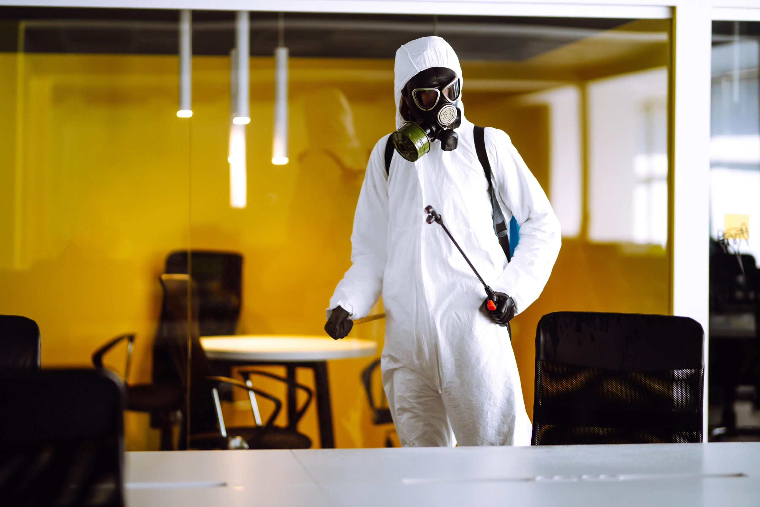 Expert pest control for commercial property shown in action by a worker in protective gear spraying an office environment.
