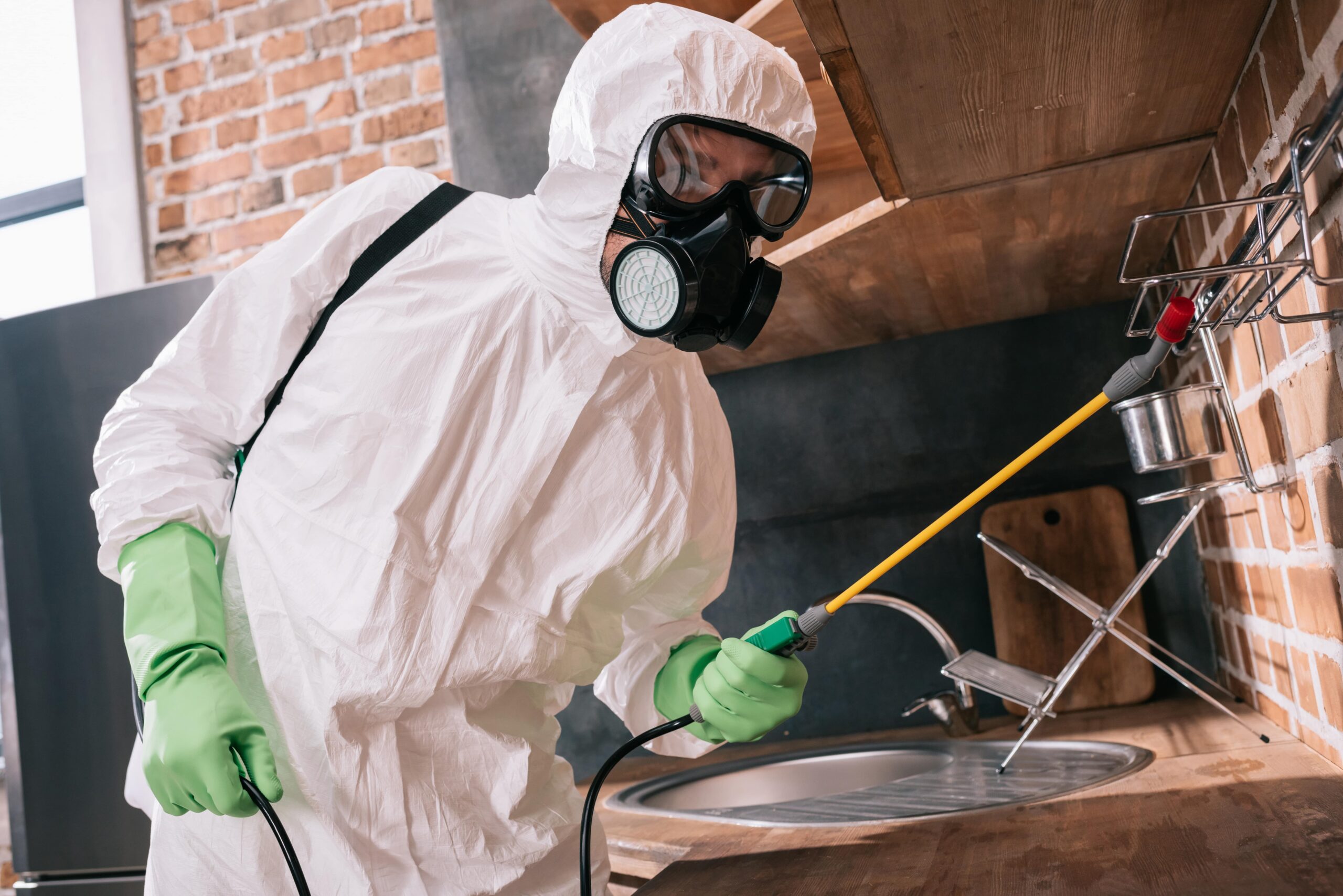 Professional pest control technician in protective gear applying termite treatment in a kitchen, showcasing effective termite treatment Dallas homeowners rely on to protect their homes.